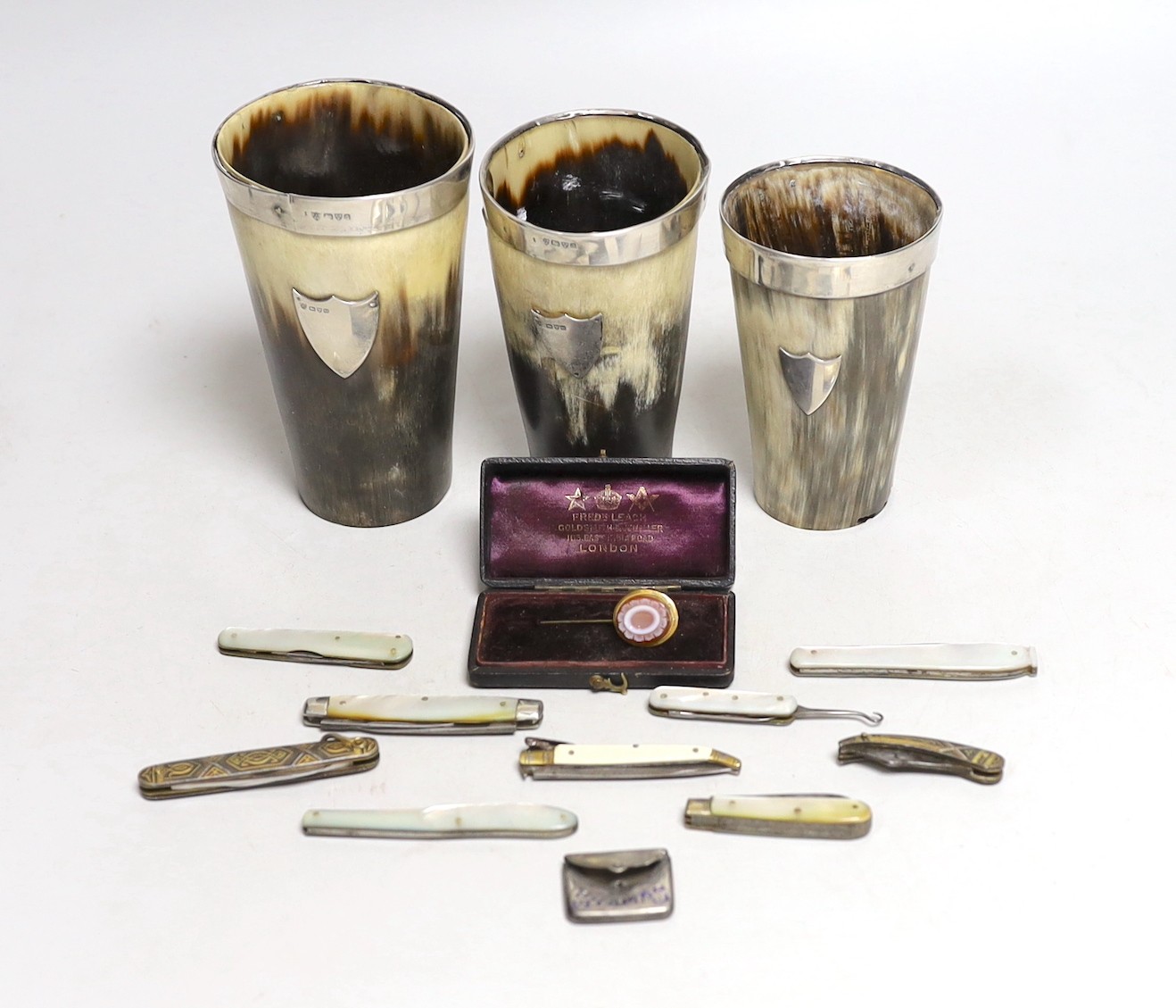 Two Edwardian silver mounted horn beakers, Haseler Brothers, Chester, 1903, largest 12.3cm, a similar Victorian beaker, a sardonyx mounted stick pin, nine assorted penknives/nail implements and an Edwardian silver and en